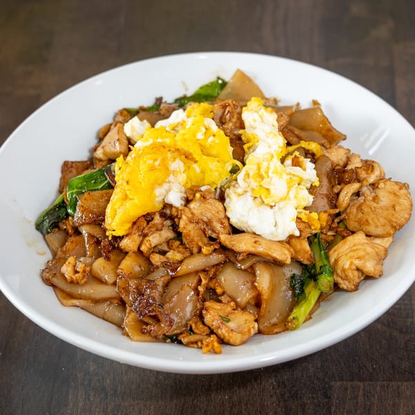 Thai Pad See Ew with wide noodles, chicken, Chinese broccoli, and scrambled egg in a white bowl.