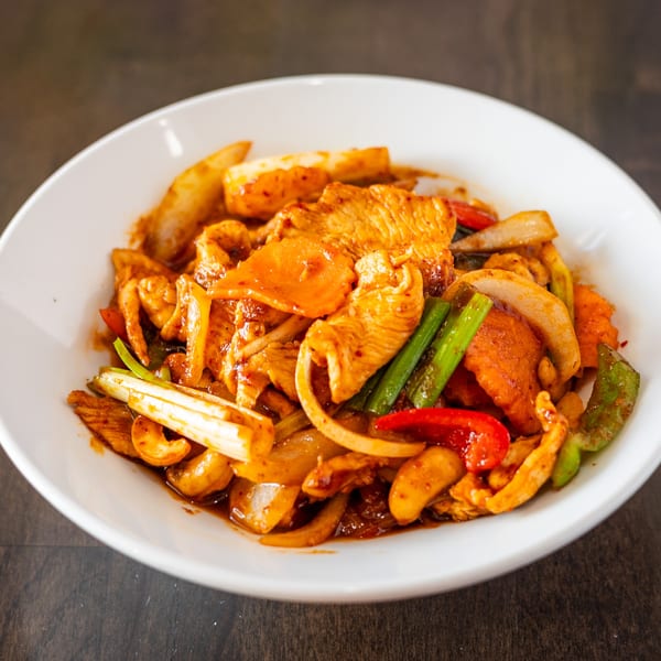 Spicy Thai cashew chicken stir-fry with vegetables in a white bowl on a dark wooden table.