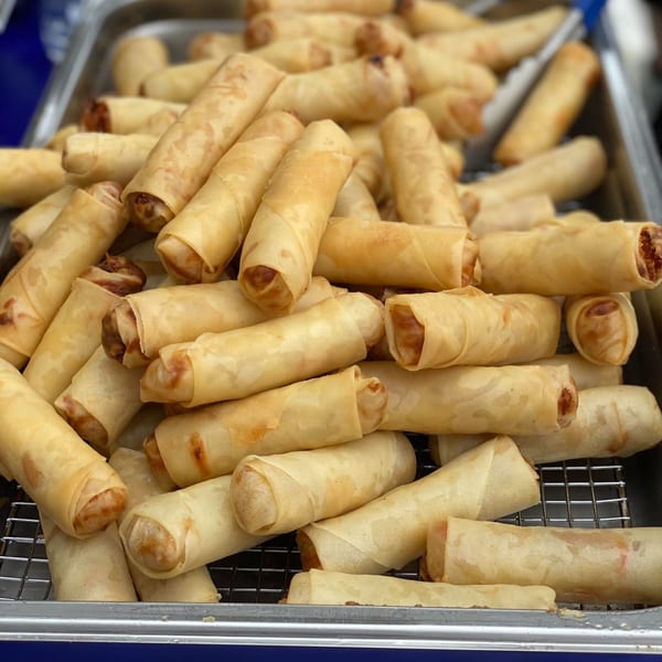 A metal tray filled with numerous golden-brown, crispy Thai spring rolls on a wire rack.