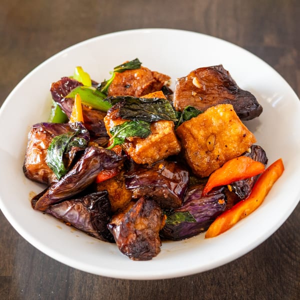 Thai eggplant and tofu stir-fry with basil and bell peppers in a white bowl.