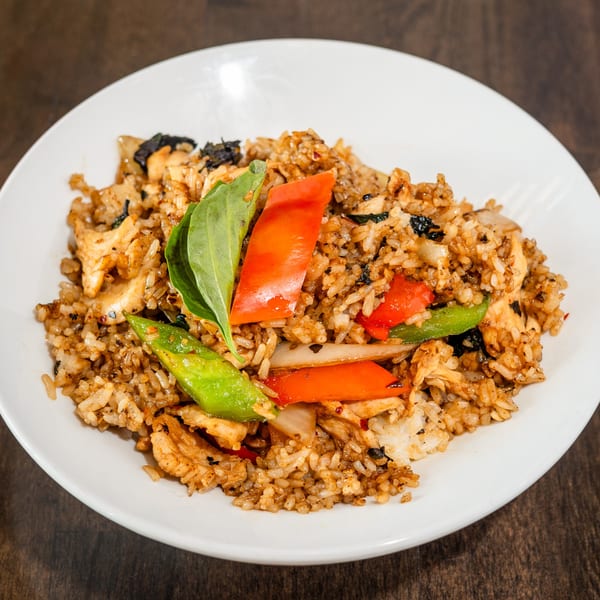 Thai fried rice with chicken, red and green bell peppers, onions, and basil on a white plate.
