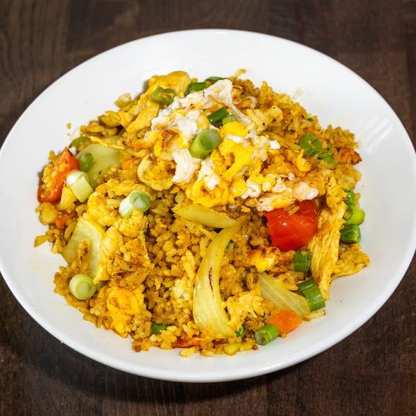 Curry fried rice with chicken, vegetables, and scrambled egg, garnished with green onions.