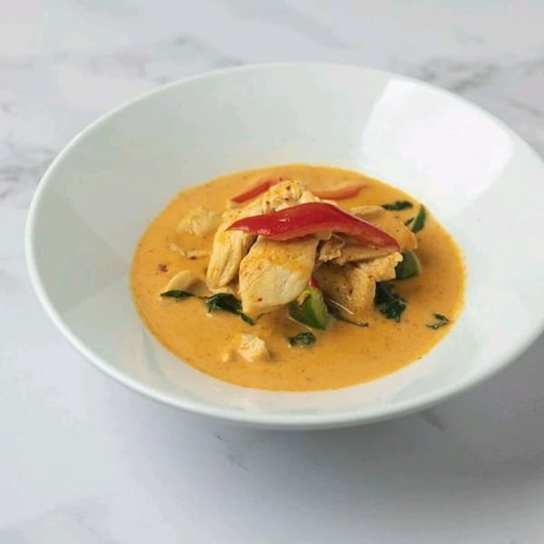 Thai red curry with chicken, red bell peppers, and basil in a white bowl.