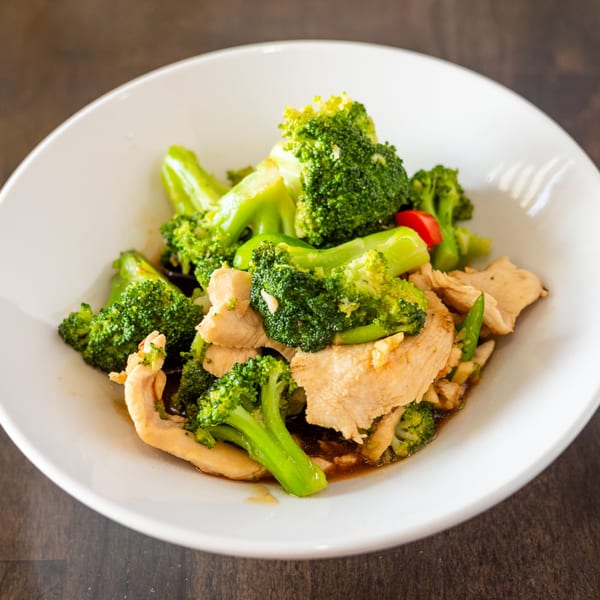 Thai chicken and broccoli stir-fry with red peppers in a white bowl.