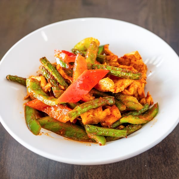 Spicy Thai stir-fry with chicken, green beans, and red bell peppers in a white bowl.