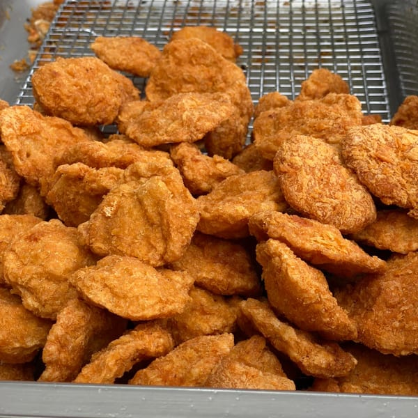 Close-up of golden-brown fried chicken nuggets piled high in a metal container with a wire rack.
