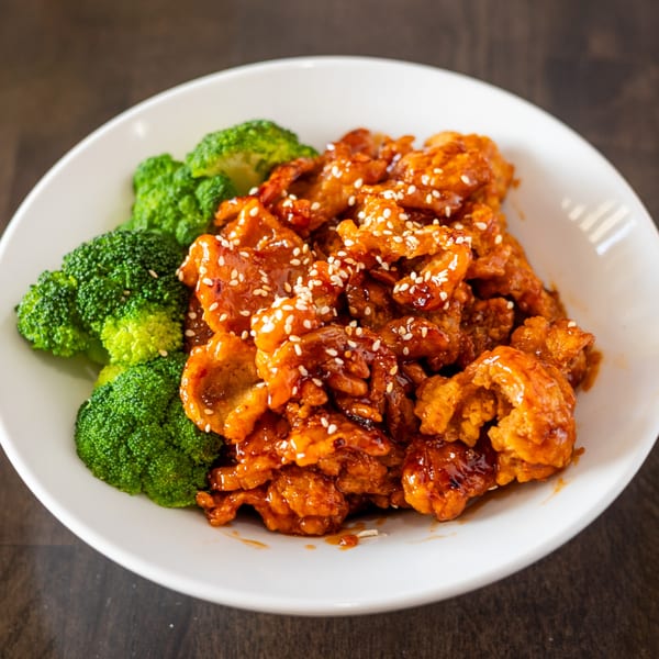 Thai Curry's orange chicken with sesame seeds and steamed broccoli in a white bowl.