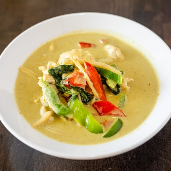 A white bowl filled with Thai green curry, chicken, red and green bell peppers, and bamboo shoots.